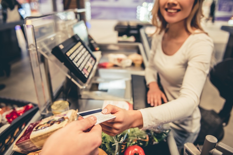 Beautiful young cashier is holding a credit card and smiling while working at the supermarket