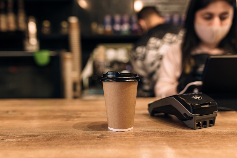 Buying a cup of coffee in a cafe, barista, NFC terminal. Blurred background. High quality photo