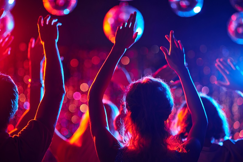 Group of young people with raised arms dancing in night club